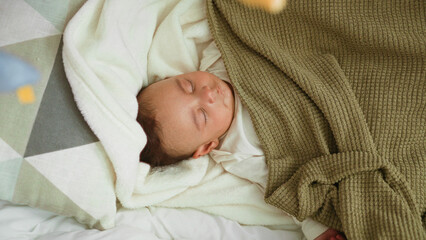 Baby sleeping on bed and cradle with bare hand peeking from under knit blanket on soft pillow in building  peaceful rest. © Krakenimages.com