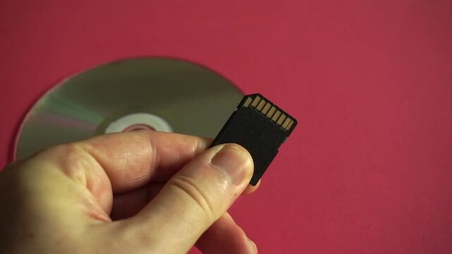 Hand holding a new sd memory card over an old compact disc, symbolizing technological evolution