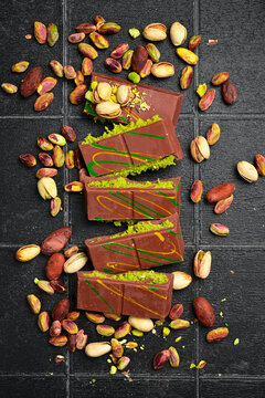 Trend Dubai chocolate with pistachio paste and kataifi. Pistachios, cocoa beans and chocolate. Top view, on a black stone background.