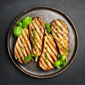 A plate of grilled eggplant. Grilled vegetables. Top view. On a gray concrete background.