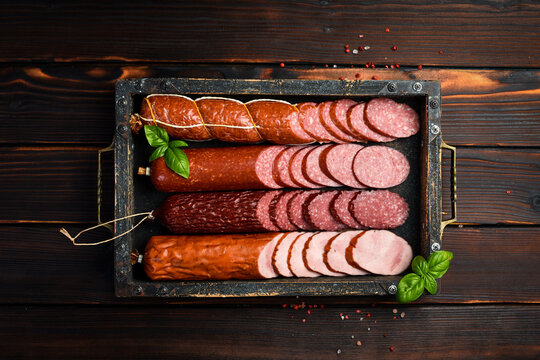 Different types of homemade smoked dry sausages on a dark wooden background. Assortment of delicious deli meats, salami and pepperoni on a tray.