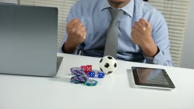 A happy and excited man sits at a computer desk, feeling euphoric because of his winning football betting bet, staring at the screen and celebrating the fantastic news, receiving the best prize.
