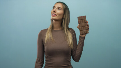 Woman holding a large chocolate bar upright while looking up in a light blue studio  pleasure craving enjoyment. © Krakenimages.com