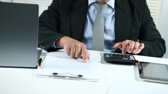 Close-up of a male accountant performing financial calculations and data analysis, using a calculator to review documents, charts, and graphs. Accounting, analytics, budgeting, investment evaluation. 