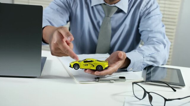A vehicle or insurance salesperson is explaining the details of a car using a miniature on the work desk to a potential client.