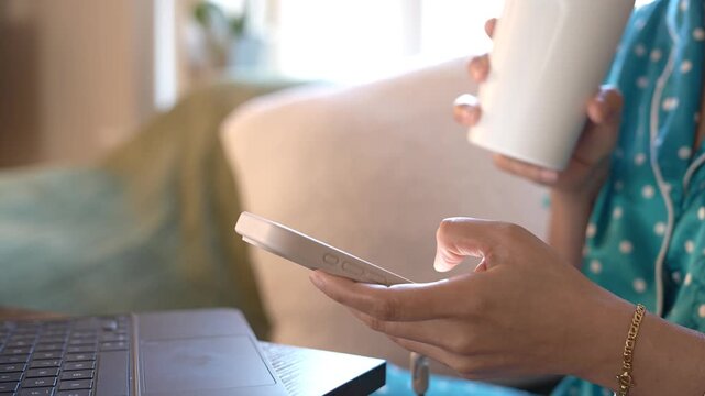 Person using smartphone and laptop while drinking coffee during morning remote work. Mobile communication, AI productivity, SaaS platform,email management,cloud workflow,multitasking,digital business 