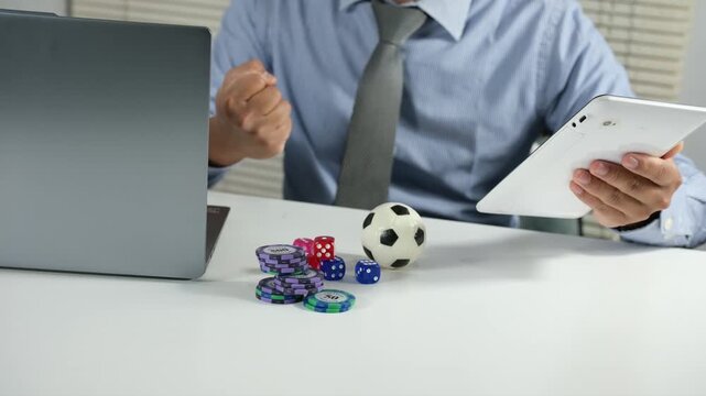 An Asian man holds a tablet computer and watches his favorite team win. He feels euphoric about winning a soccer bet, staring at the screen and celebrating the fantastic news, receiving the best prize