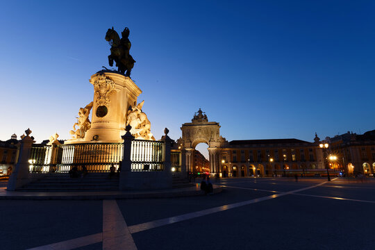 Dramatic dusk view of Lisbon Comercio square , with the illuminated equestrian statue of King Jose I rising in silhouette against a deep cobalt blue sky .