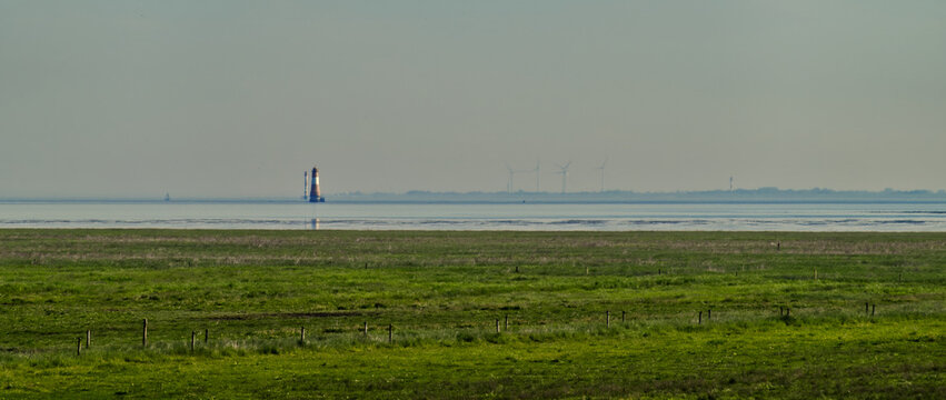 Dangast lighthouse standing amidst the wadden sea, green marshland foreground, distant wind turbines generating clean energy