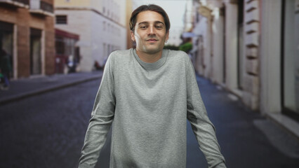 Man shrugging shoulders with closed eyes in a grey sweater on a cobblestone street, slight smirk and relaxed stance  uncertainty. © Krakenimages.com