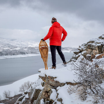 man with classic Huron snowshoes is overlooking a mountain lake in winter scenery - Horsetooth Reservoir in northern Colorado