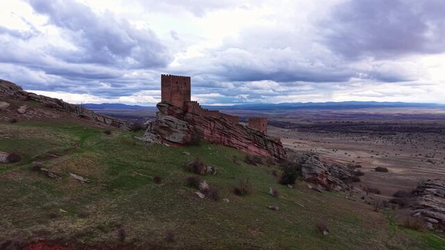 Fortified stone keep of Castillo de Zafra rising from banded red and grey sandstone, overlooking vast open plains under dramatic cloudy sky, Guadalajara, Castilla-La Mancha, Spain