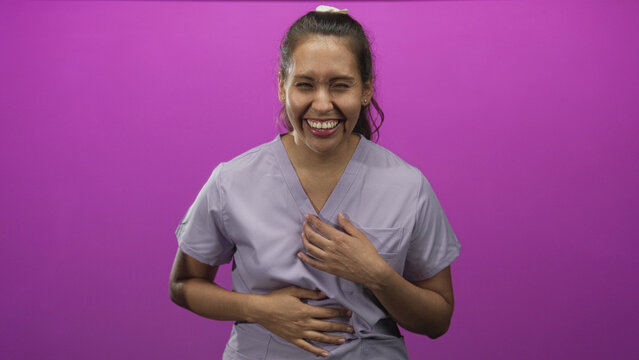 Woman laughing with hand over mouth and hands clasped on stomach in a purple studio; joy playfulness warmth.