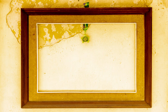
Empty Vintage Wooden Frame On Peeling Yellow Wall With Hanging Green Ornament And Blank Space
