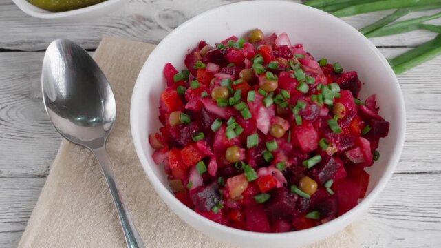 Smooth camera movement showing a rustic table setting with a metal spoon, bowl of homemade vinaigrette salad made with beetroot, potatoes, carrots, peas, and pickles and a plate of sliced bread