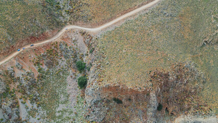 Top down aerial view of tourist cars driving on winding dirt road along steep mountain rocky slopes of Greece Mediterranean region in summer © moryachka