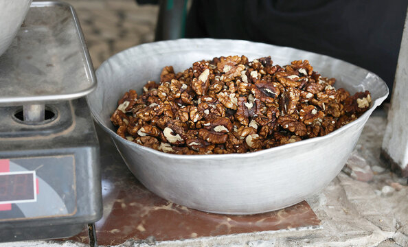 Fresh walnut kernels displayed in a large metal bowl at a traditional farmers market. Healthy natural food rich in protein and omega fats, offered for sale in bulk at a local market.