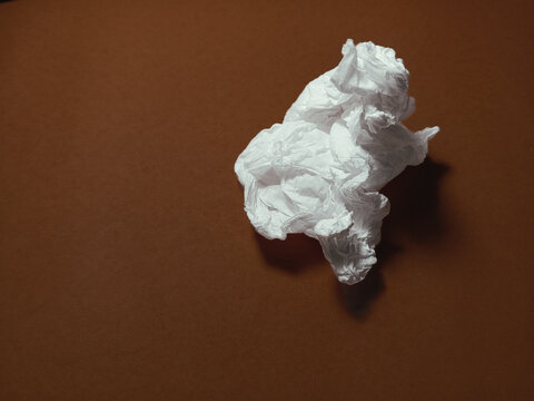 Minimalist top view of a crumpled white tissue paper on dark brown background