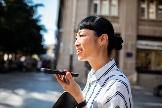 Smiling businesswoman using voice command on smartphone in city street