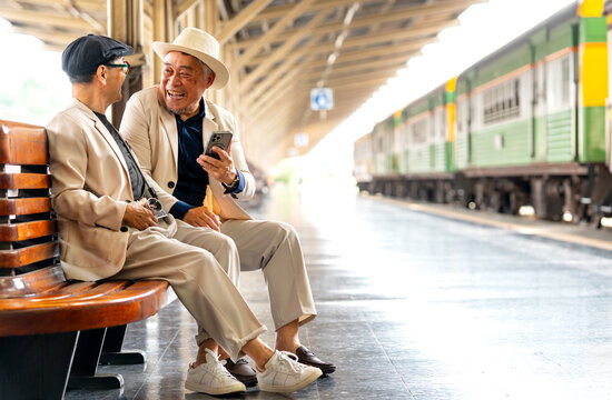 Couple Asian senior lover of lgbtq sit on long bench in train station and look fun or enjoy together near the train.