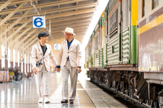 Couple Asian senior lover of lgbtq walk together near train locomotives with happiness.