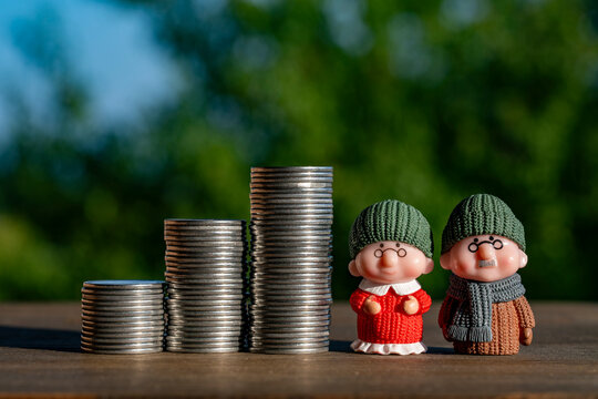 Miniature senior couple figures standing next growing coin stacks on green background, closeup. Financial concept of retirement planning, senior pension savings, old age security, or family budget