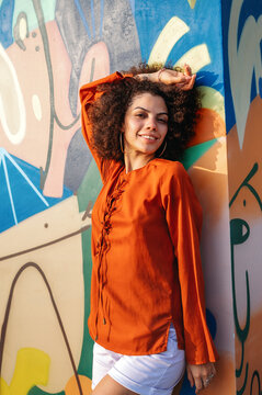 Architectural elements meet urban art as a young happy woman stands against a textured wall