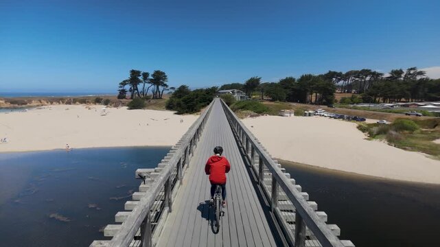 A mature woman rides her bike across Pudding Creek trestle bridge in Fort Bragg. The sun shines bright on this beautiful day.