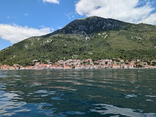 Fototapeta premium Sunny coastal panorama of Perast with crystal clear Adriatic water and mountain backdrop in Montenegro