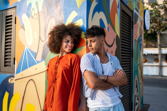 Stylish young couple in trendy summer outfits posing together by a colorful artistic city wall