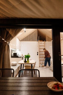 Vertical woman cleaning modern tiny cabin floor with mop during evening housekeeping