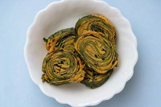 Top view of traditional Indian snack Alu Vadi or Patra (steamed colocasia leaves roll) in a white bowl against a blue background