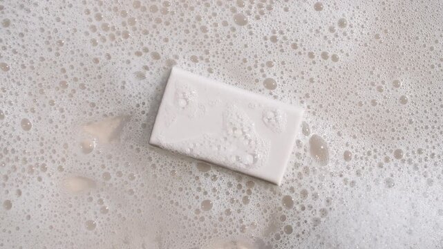 A bar of soap on a water surface with bubbles of white soapy foam. Concept of bath products, skin care products advertisement spa cosmetics. Body care and relaxation. High quality 4k footage