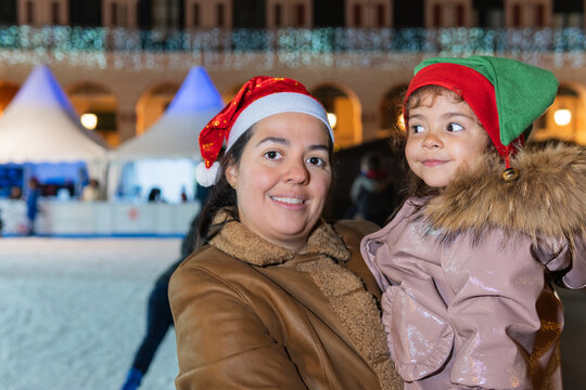Happy mother holding her child with elf hat at a festive ice rink