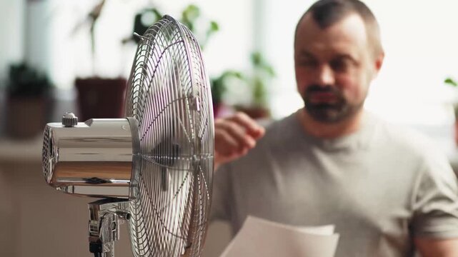 Exhausted man suffering from headache near fan in heatwave