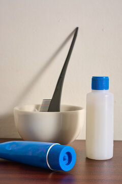 hair dye kit on wooden table top, blue color tube with developer bottle and tinting brush in ceramic bowl, side view with copy space, salon hair coloring treatment
