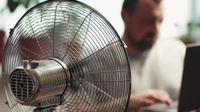 Freelancer working on laptop near electric fan at home