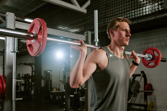Young adult Caucasian man lifting barbell in gym, training strength and fitness with focused posture. Ideal for workout programs, personal training, healthy lifestyle marketing