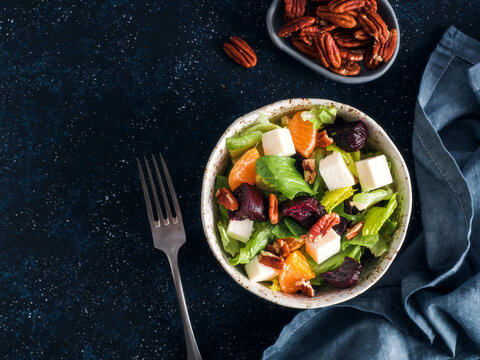 Healthy winter salad with beet cubes, feta cheese, orange segments and pecans in bowl. Flat lay on dark textured background with copy space. Perfect for restaurant menu or organic diet blog. Top view