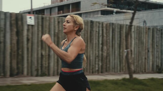 Determined female runner sprinting past wooden fence on cloudy morning