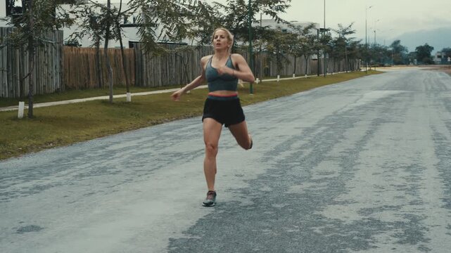 Woman jogging on quiet tree lined street past streetlights under cloudy sky