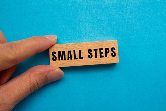 Hand holding a wooden block with small steps on blue background, illustrating progress, motivation, and goal achievement through incremental actions
