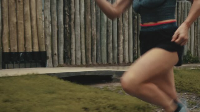 Female runner's thighs and legs in motion beside wooden fence and lawn