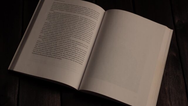 Close-up of a hand turning pages of an open book lying on a wooden table. Concept of reading, education, literature, studying, relaxation, and knowledge