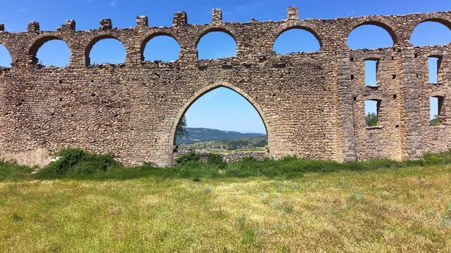 Medieval Gothic pointed arch in a ruined stone aqueduct wall near Morella, Castellon, Spain, framing a green valley and blue sky