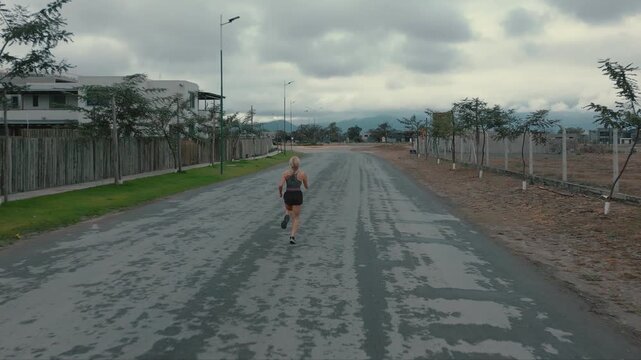 Elevated back view of female runner approaching distant buildings on paved road