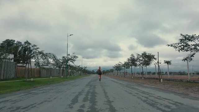 Woman running away down long straight road beneath cloudy sky
