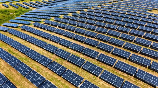 Close high angle shot of structured solar panel rows. High angle detailed shot of parallel rows of blue solar panels installed on dry grassy ground.