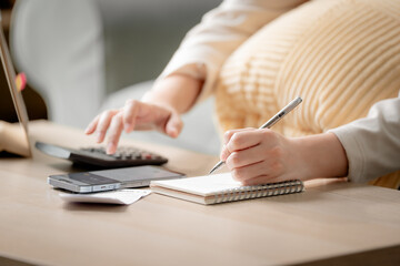 Fototapeta premium Personal budgeting concept. Anonymous person calculating household expenses with calculator while writing notes beside smartphone at home. Budget, finance, savings, planning, expenses