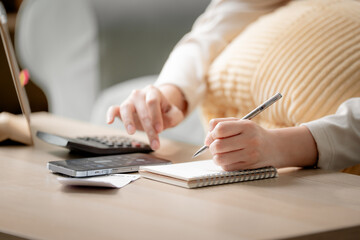 Fototapeta premium Personal budgeting concept. Anonymous person calculating household expenses with calculator while writing notes beside smartphone at home. Budget, finance, savings, planning, expenses